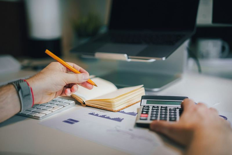 Hands with a pencil and a calculator over printed charts at a desk